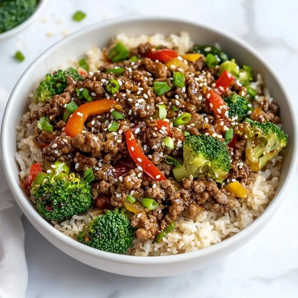 Ground Beef and Broccoli Stir Fry, quick beef stir fry, healthy broccoli dinner, easy weeknight stir-fry, family-friendly beef and broccoli The dish is served in a large white bowl placed on a white marbled surface. The base layer is light brown cooked rice spread evenly around the bowl. On top of the rice, there are pieces of cooked ground beef that appear dark brown and juicy, mixed with bright green broccoli florets and vibrant red bell pepper slices. There are small bits of green onions scattered throughout the dish, adding fresh green specks. White sesame seeds are sprinkled over the beef, adding texture and contrast. The overall look is colorful and fresh, with a mix of soft, tender, and crisp textures.