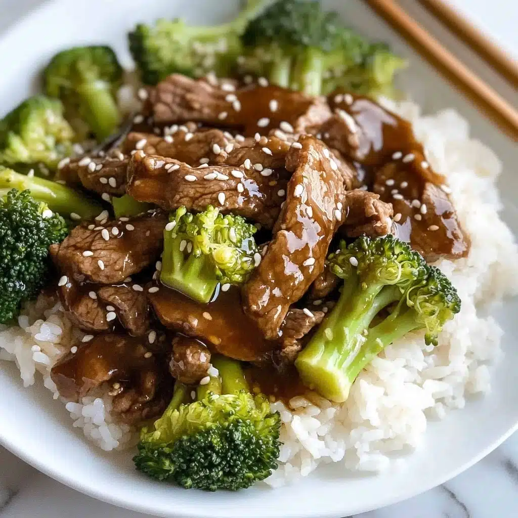 Chinese Beef and Broccoli, Chinese beef and broccoli stir-fry, beef and broccoli recipe, Chinese stir-fry recipes, quick beef stir-fry A white plate holds a serving of white rice as the base layer, topped with bright green broccoli pieces and brown slices of beef. Both the beef and broccoli are coated in a shiny, thick brown sauce, sprinkled with small white sesame seeds. The broccoli pieces show a bumpy texture on top with smooth stems, and the beef slices have a slightly rough texture with a glossy finish from the sauce. The food is placed on a white marbled tabletop with wooden chopsticks resting on the edge of the plate.
