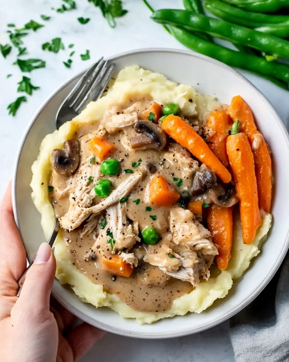 A white bowl holds a plate of food with three visible layers: the bottom layer is mashed potatoes in a creamy light yellow color with a soft texture; above this is a thick layer of shredded light brown chicken and whole small orange carrots mixed in a beige sauce with visible pepper flakes and small chunks of mushrooms and celery; on the side, fresh bright green beans lie next to the chicken and mashed potato mix. The food is garnished with scattered chopped green herbs. A woman's hand is holding the bowl from the lower left corner. The background is a white marbled surface with some scattered herbs and a silver fork rests on the bowl s edge. photo taken with an iphone --ar 4:5 --v 6.1