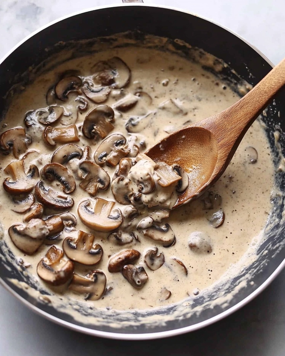A white plate is held by a woman's hands, showing a thick piece of cooked meat with a dark brown, slightly charred crust. The meat is covered with a creamy mushroom sauce that has light beige color and slices of soft, pale brown mushrooms. On top of the sauce, there is a small fresh green herb garnish. A silver fork rests on the plate touching the meat and sauce. In the background, there is a white plate with more mushroom sauce and mushrooms, all placed on a white marbled surface. Photo taken with an iphone --ar 4:5 --v 6.1