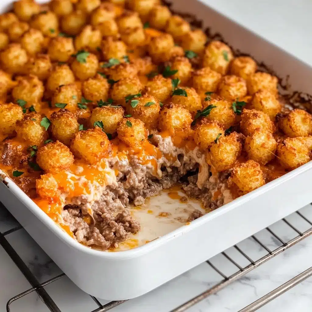 Tater Tot Casserole, Tater Tot casserole recipe, cheesy tater tot casserole, easy comfort food, hearty dinner ideas The image shows a white rectangular baking dish with a layered casserole inside. The top layer is covered with golden-orange roasted tater tots sprinkled with small pieces of green herbs. Beneath the tater tots is a browned layer of ground beef mixed with a creamy white sauce. A portion of the casserole is scooped out from one corner, revealing the two distinct layers. The dish sits on a metal wire rack, all placed on a white marbled surface.