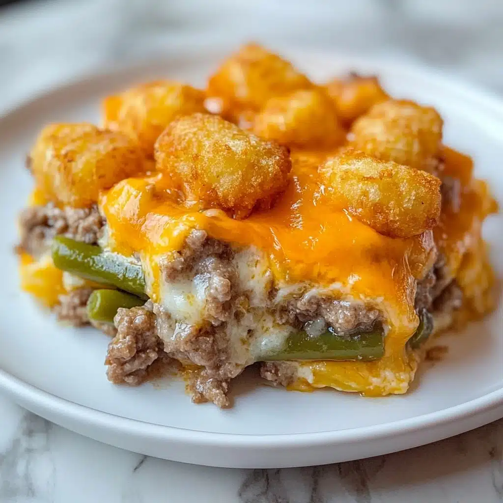 Tater Tot Casserole, Tater Tot casserole recipe, cheesy tater tot casserole, easy comfort food, hearty dinner ideas The dish is made in three clear layers, all on a white plate on a white marbled surface. The bottom layer is a mix of cooked ground meat with diced onions, visible in a creamy white sauce with some melted cheddar cheese. The middle layer consists of green beans covered with melted cheddar cheese, adding a yellow-orange color in the middle. The top layer is made of golden brown, crispy tater tots, arranged neatly and evenly on top, some sitting on the cheesy middle layer. The cheese is melted and slightly stretching between the layers, giving a warm and tasty look.