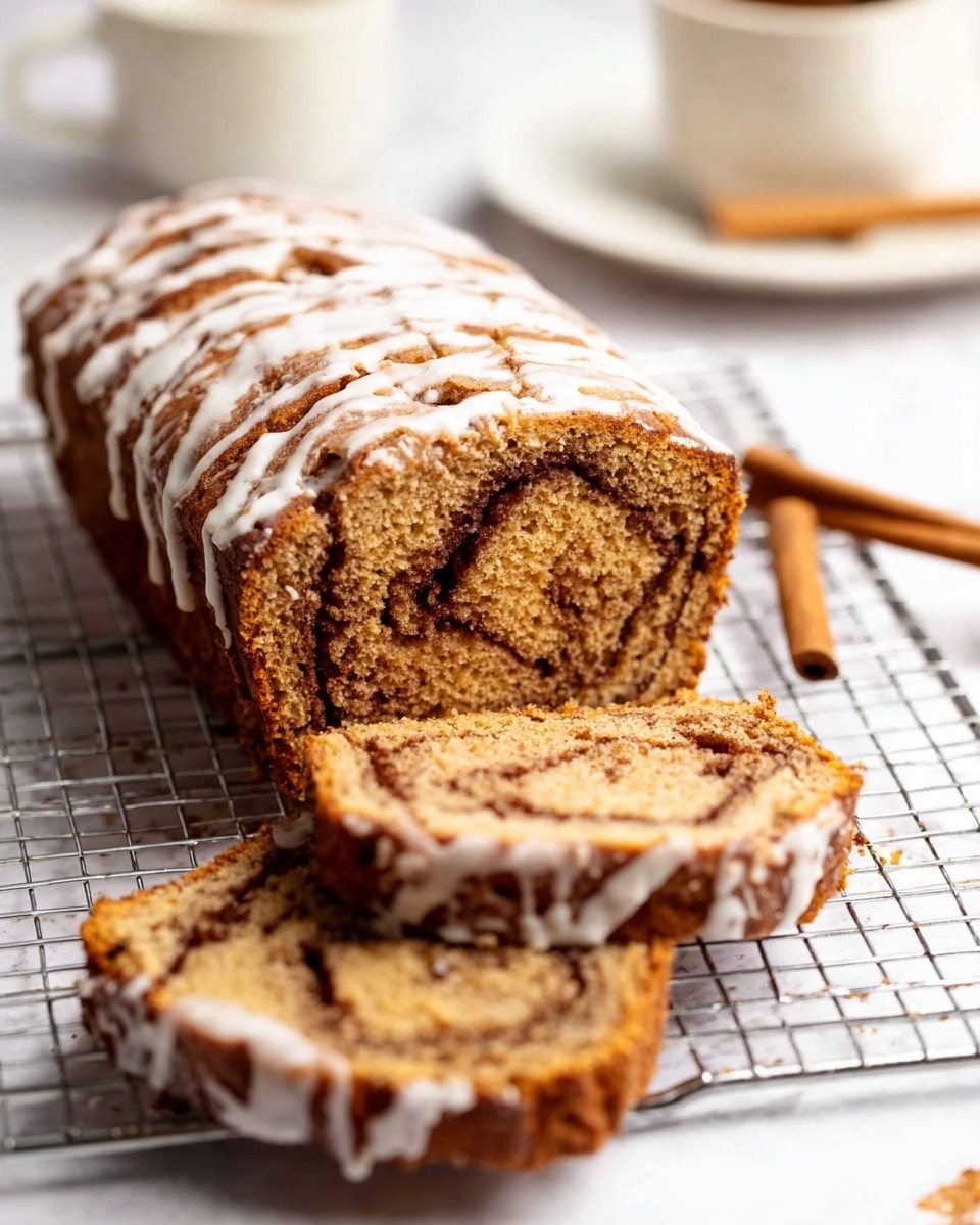The image shows a loaf of cinnamon swirl bread with two slices placed in front of it on a cooling rack. The bread has a warm brown color with visible darker cinnamon swirls running through each slice. The top of the loaf and slices have a light drizzle of white icing that contrasts with the brown bread. Behind the bread, there is a white plate on a white marbled surface with a small cup and a cinnamon stick blurred in the background. The texture of the bread looks soft and moist with the swirl pattern clearly visible throughout the slices. photo taken with an iphone --ar 4:5 --v 7
