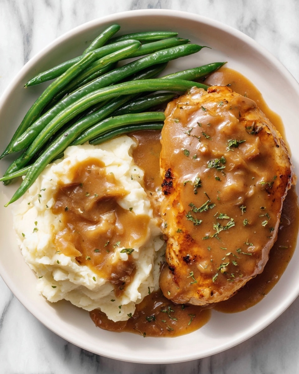 A white plate with three main parts: on the left, bright green cooked green beans with a smooth texture; in the center, creamy white mashed potatoes topped with a thick brown gravy that covers most of the potatoes and has small bits of food mixed in; on the right, a large piece of golden-brown cooked meat covered in the same thick brown gravy with some green herb pieces sprinkled on top; the plate is placed on a white marbled surface. photo taken with an iphone --ar 4:5 --v 7