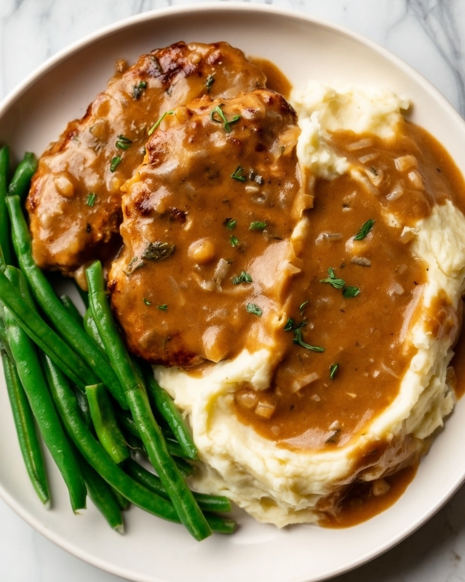 The image shows a white plate with three sections of food. On the right side, there is a smooth, creamy mashed potato layer with a light beige color, topped with a thick, rich brown gravy that has small pieces of herbs and sauce spread evenly. To the left, there are two pieces of golden brown meat covered in the same brown gravy with visible herbs. On the bottom left, bright green cooked green beans are placed in a neat pile. The plate is set on a white marbled surface. Photo taken with an iphone --ar 4:5 --v 7