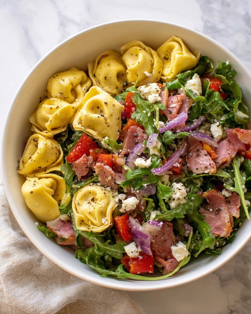A white bowl filled with three main layers: at the bottom, a layer of yellow tortellini pasta with smooth, soft texture; above that, scattered pieces of red bell pepper cubes and small chunks of pinkish cured meat; on top, fresh green arugula leaves mixed with small white cheese crumbles and thin slices of red onion, all lightly sprinkled with black pepper. The bowl is set on a white marbled surface with a soft cloth partially visible to the side. Photo taken with an iphone --ar 4:5 --v 7
