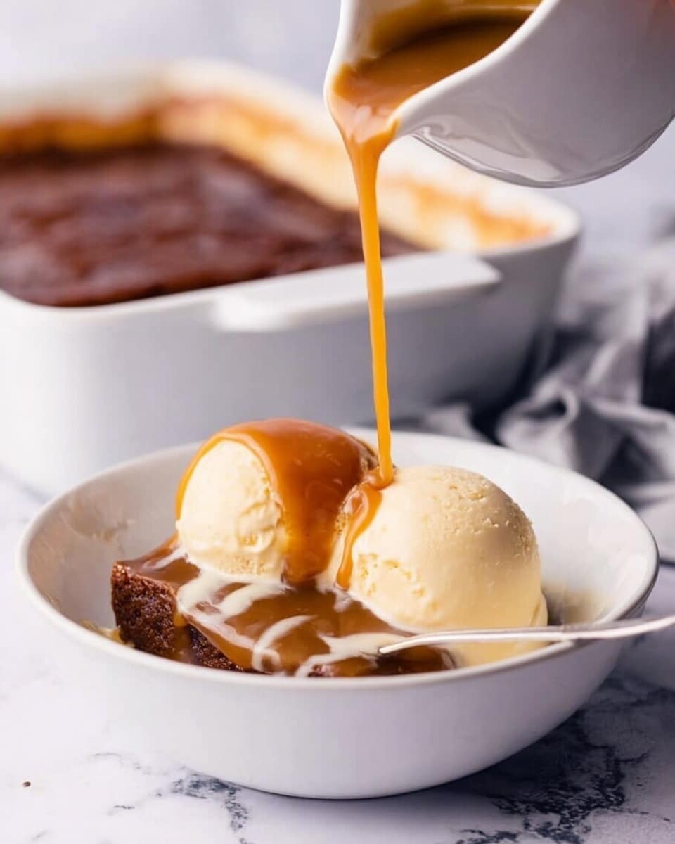 A white bowl on a white marbled surface holds two scoops of smooth, pale vanilla ice cream on one side, with a thick, dark brown dessert base beside it. A woman's hand pours warm caramel sauce from a white small pitcher, the caramel flowing in a thick stream onto the dark dessert. A silver spoon rests inside the bowl. In the background, a white baking dish with the same dark dessert is slightly out of focus. Photo taken with an iphone --ar 4:5 --v 7