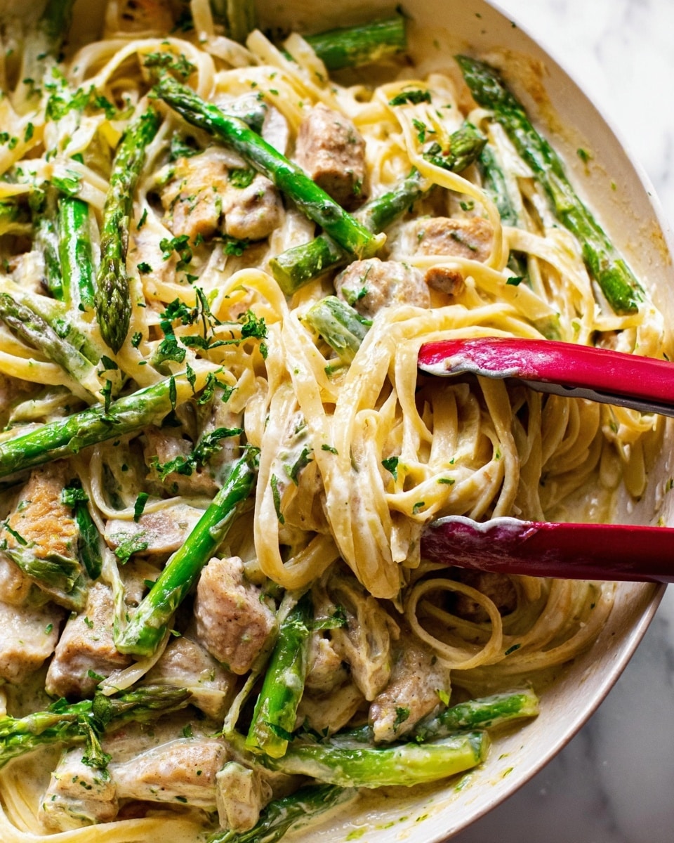 This close-up image shows a creamy pasta dish with three main layers. The bottom layer is creamy white sauce mixed with cooked light beige pasta noodles that are long and smooth. On top of the pasta, there are bright green asparagus spears scattered around, slightly cooked to show a tender texture with small darker green tips. The top layer has medium-sized, light brown meat pieces mixed evenly throughout. Some finely chopped green herbs are sprinkled on everything, adding a fresh touch. Red tongs grip some pasta and asparagus on the right side. The whole dish is in a white bowl, sitting on a white marbled surface. Photo taken with an iphone --ar 4:5 --v 7