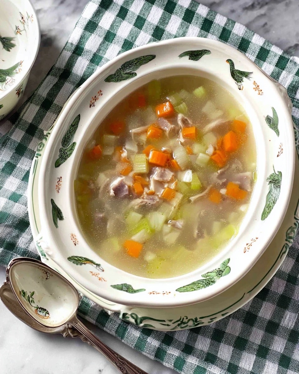 A white ceramic serving dish with green and blue bird and leaf designs holds a clear soup with small chunks of light orange carrots, pale yellow celery, translucent white onions, and small pieces of light brown meat floating in the broth. The dish is placed on a white marbled surface with a green and white checkered cloth underneath, and two tarnished silver spoons lay nearby. A white ladle with matching bird and leaf designs rests beside the dish. Photo taken with an iphone --ar 4:5 --v 7