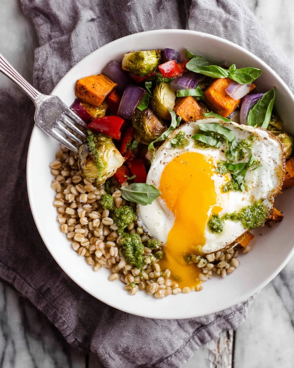 A white bowl is filled with three main layers: on the left side, cooked wheat berries with a light brown color and slightly rough texture; on the right side, a mix of roasted vegetables including small green Brussels sprout halves, bright red bell pepper pieces, purple onion chunks, and orange sweet potato cubes, all slightly browned and glossy; on top sits a fried egg with a runny bright yellow yolk breaking open, soft white edges, and a green sauce drizzled over it, garnished with thinly sliced fresh basil. A fork is lifting part of the egg, letting the yolk drip down. The bowl rests on a crumpled gray cloth over a white marbled surface. Photo taken with an iphone --ar 4:5 --v 7
