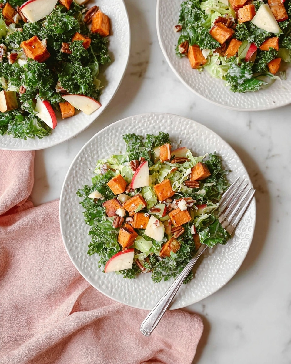 The image shows a fresh salad served on three white plates with textured edges placed on a white marbled surface. The salad has a base of dark green curly kale leaves mixed with light green shredded Brussels sprouts. There are medium-sized orange roasted sweet potato cubes scattered on top along with small chunks of red and white apple pieces. Small bits of creamy white cheese and some reddish-brown pecan nuts add texture and color contrast. A silver fork rests diagonally on the bottom white plate near a soft pink cloth napkin. The overall look is bright and healthy with a mix of rough and smooth textures. photo taken with an iphone --ar 4:5 --v 7