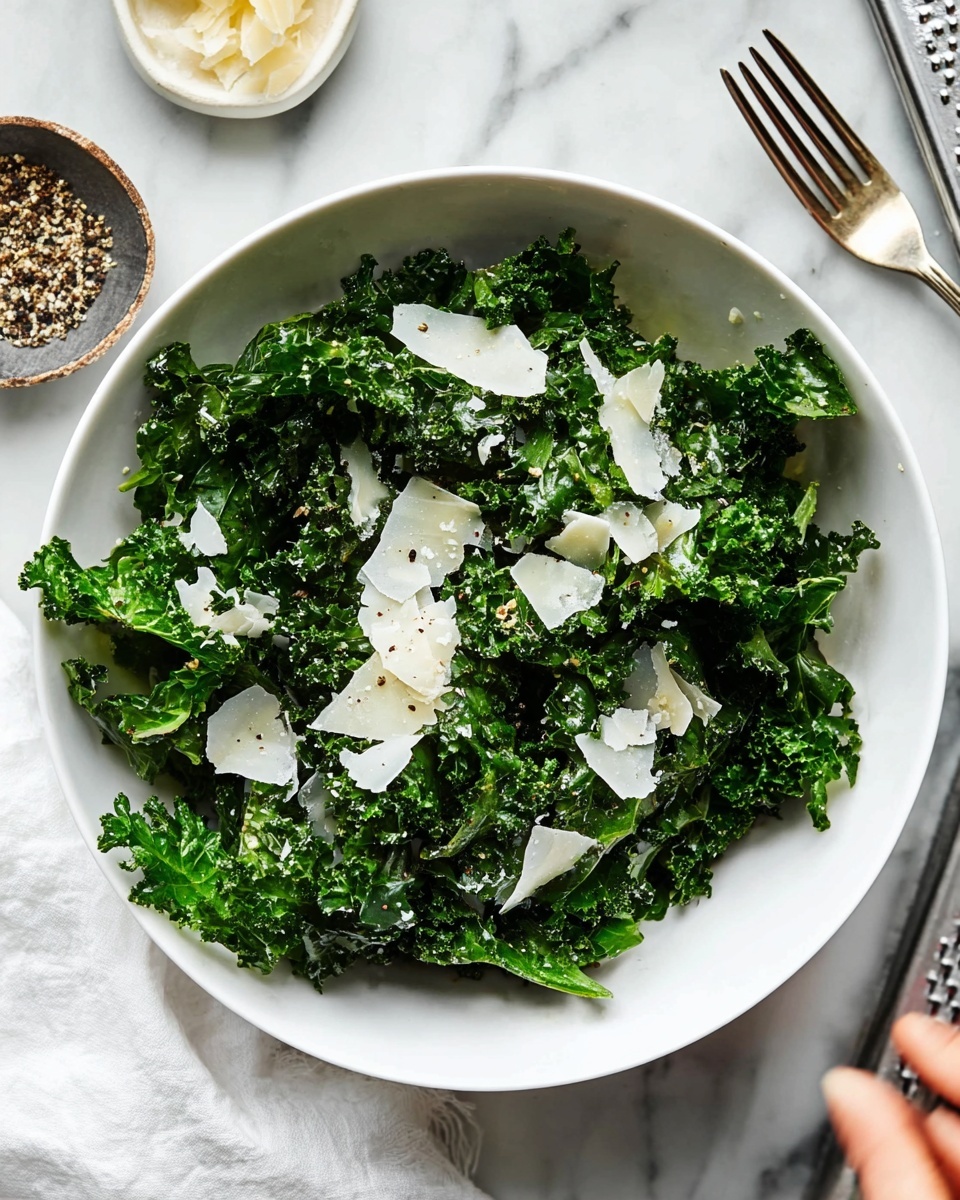 A white plate filled with fresh green kale leaves as the base layer, topped with thin, uneven white shavings of cheese scattered across the greens. A silver fork rests on the right side of the plate, partially on top of the kale. The plate is placed on a white marbled surface with a small bowl containing salt and black pepper in the upper left corner of the image. A white and black checkered cloth is partially visible at the bottom left. Another white plate with a similar kale and cheese salad is partially seen in the upper right corner. photo taken with an iphone --ar 4:5 --v 7