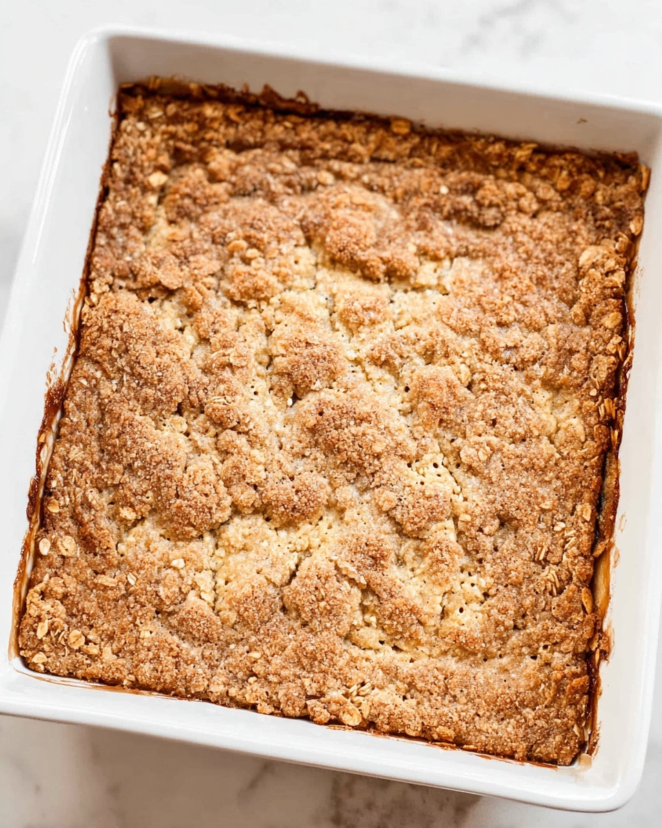 A piece of apple crumble dessert is shown on a white plate, placed over another white plate on a white marbled surface. The bottom layer is a golden brown crumbly crust with a rough texture. Above it is a layer of soft cooked apple chunks in a shiny caramel sauce, with some more crumbly bits on top. The dessert is finished with a generous swirl of white whipped cream dusted with a light sprinkle of cinnamon. Photo taken with an iphone --ar 4:5 --v 7