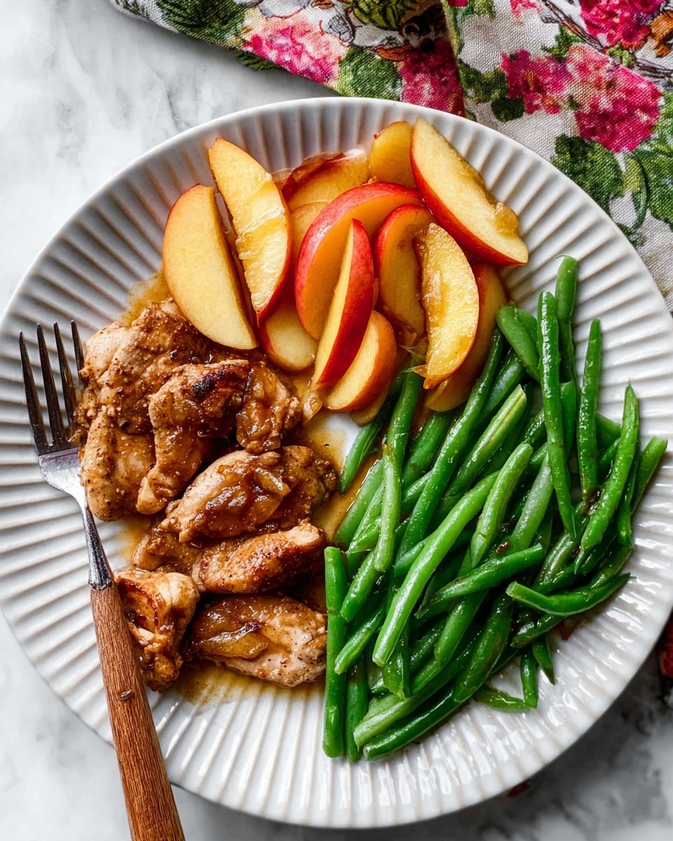 A white plate with ridged edges holds a meal arranged in three parts: on the left side, there are three pieces of browned cooked chicken with a slightly crispy texture, mixed and topped with slices of cooked yellow and red apple wedges displaying a glistening sauce; on the right side, a neat pile of bright green steamed string beans with a smooth, shiny surface is placed; a fork with a wooden handle rests on the plate's bottom left side. The plate is set on a white marbled surface with a floral cloth partially visible in the upper right corner. Photo taken with an iphone --ar 4:5 --v 7