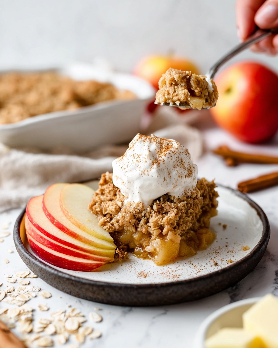 The image shows a white square baking dish filled with a baked oatmeal dish, cut into six pieces. The top layer is golden brown with visible oats and small apple chunks scattered throughout. On each cut piece, there are thin slices of red and yellow apples arranged in a fan shape, adding a fresh look to the warm baked texture. Around the baking dish, there are whole and sliced apples, a knife, a glass of dark liquid, cinnamon sticks on white plates, all placed on a soft peach-colored cloth over a white marbled surface. photo taken with an iphone --ar 4:5 --v 7