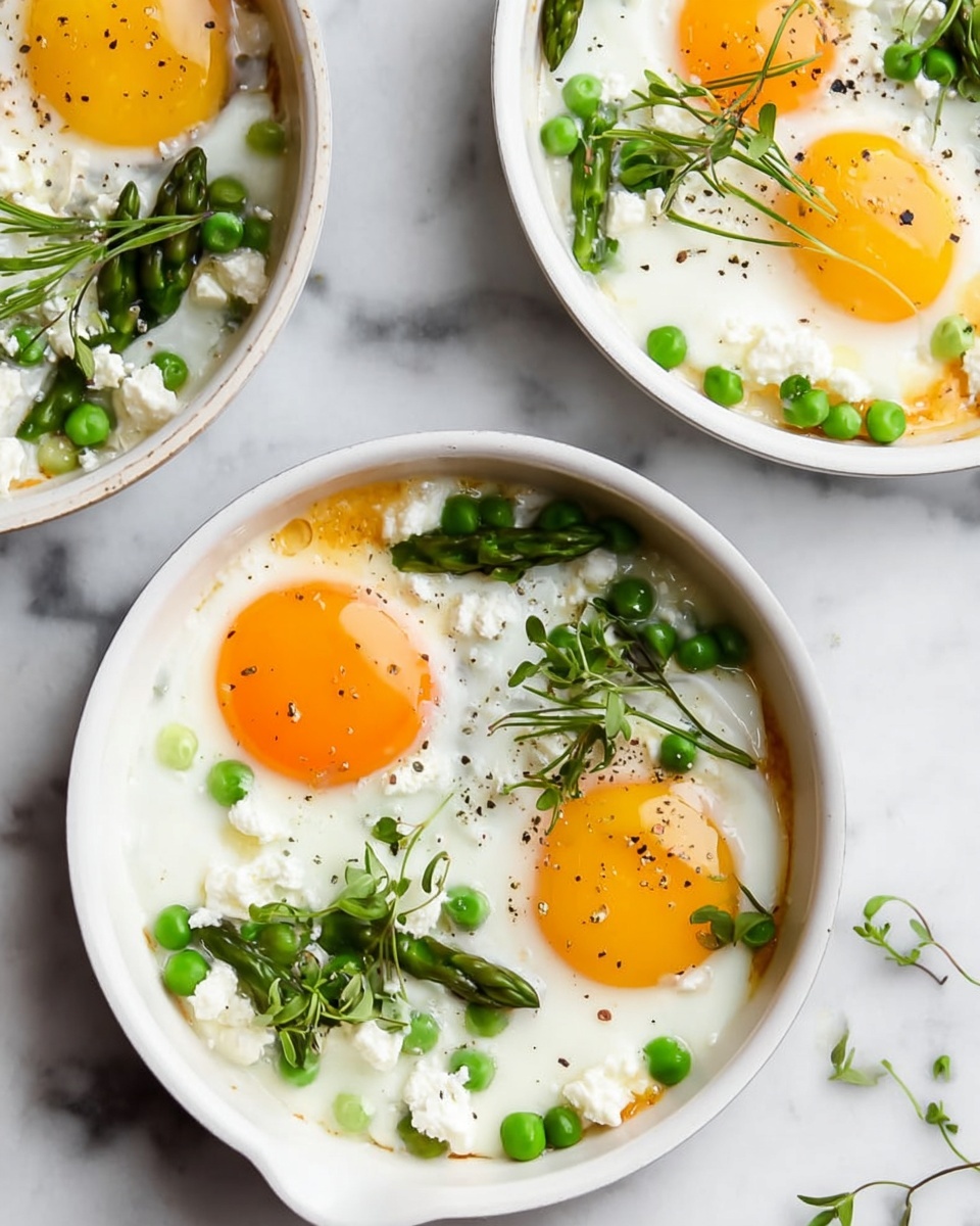The image shows three white pans with fried eggs. Each pan has eggs with bright yellow and orange yolks sitting on smooth, white egg whites. The eggs are topped with small pieces of green asparagus, bright green peas, and white crumbled cheese. There are also tiny green chives and microgreens sprinkled on top. The pans are on a white marbled surface, and the edges of the pans are simple and clean. The focus is on the fresh, colorful ingredients on the eggs. photo taken with an iphone --ar 4:5 --v 7