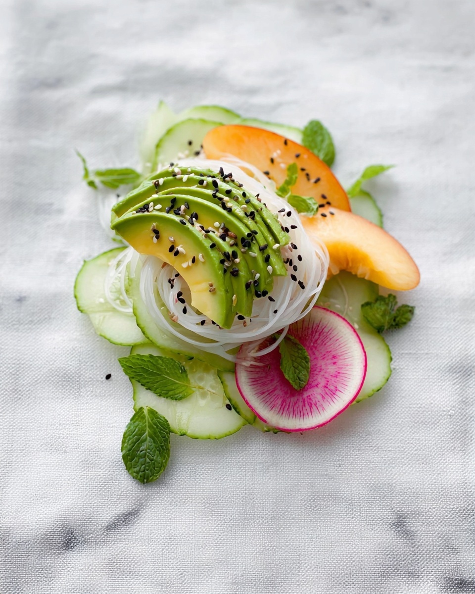 The image shows a small stack of fresh, thin cucumber slices at the bottom, light green with a smooth texture and slightly curved edges. On top, there are a few thin white noodle strands loosely placed, adding a soft texture. Centered on the noodles is a fan of avocado slices, bright green with a creamy texture, sprinkled with black and white sesame seeds. Around the avocado, there are small dark green basil leaves and bright green mint leaves for a fresh look. To the right, a thin slice of peach shows a soft orange and pink gradient with a smooth surface. Underneath all these layers is a thin round slice of watermelon radish with a white outer edge and a pink center. The dish is arranged on a white marbled surface. photo taken with an iphone --ar 4:5 --v 7