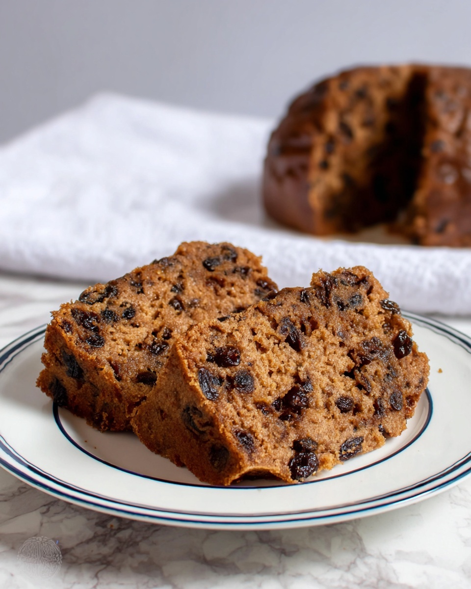 The image shows two thick slices of a dense brown cake with dark spots of raisins spread evenly throughout the cake layers, placed side by side on a white plate with blue rings around the edge. The texture looks moist and slightly crumbly with small chunks of raisins visible inside. In the background, there is a larger piece of the same cake, partially blurred, resting on a white cloth. The surface beneath the plate is a white marbled texture. Photo taken with an iphone --ar 4:5 --v 7