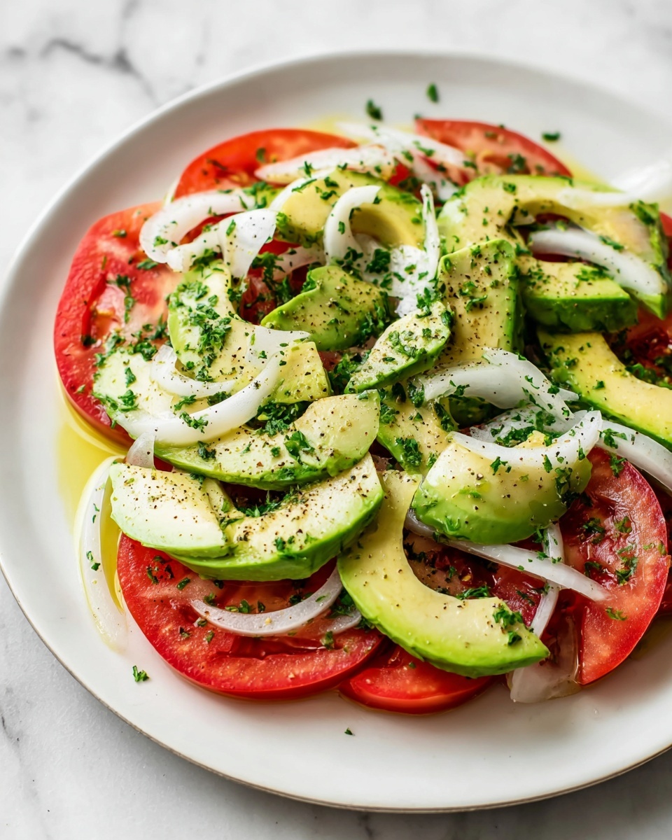 The dish shows a white plate with a layer of red tomato slices arranged around the edge, topped by a layer of light green avocado slices placed in the middle, creating a circular pattern. Thin slices of white onion are scattered evenly on top of the avocado. The salad is sprinkled with chopped green herbs and small black seeds, adding texture and color contrast. The plate is on a white marbled surface, with a bunch of fresh green parsley and white utensils nearby. A woman's hand is slightly visible on the side of the plate. Photo taken with an iphone --ar 4:5 --v 7