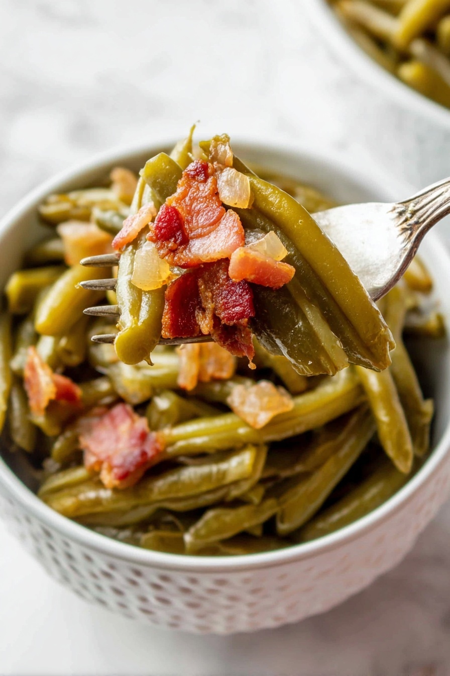 A white bowl with a pattern holds cooked green beans layered at the bottom, soft and shiny with a slightly wrinkled texture. On top, small chunky pieces of browned bacon with a reddish-brown tone and a bit of translucent cooked onion are mixed in. A fork lifts some green beans and bacon from the bowl, showing the layers clearly, with the vegetables still moist and the bacon crispy in places. The background is a white marbled surface. photo taken with an iphone --ar 2:3 --v 7 - Slow Cooker Green Beans with Bacon, green beans and bacon recipe, crockpot green beans, savory green bean side dish, easy green beans with bacon