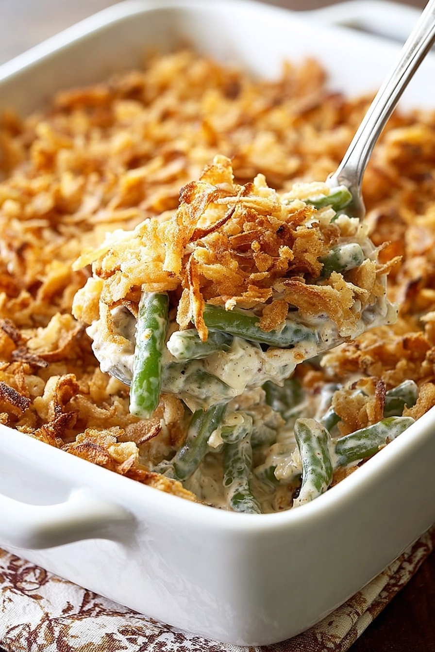 A white rectangular baking dish filled with a creamy green bean casserole topped with a thick layer of crispy golden brown fried onions. The casserole shows soft green beans mixed with a light beige creamy sauce beneath the crunchy topping. In the foreground, a white spoon lifts a serving, revealing the creamy texture mixed with green beans and bits of fried onions. The dish is placed on a table with a white marbled texture showing under the edges. Photo taken with an iphone --ar 2:3 --v 7 - Green Bean Casserole with Bacon and Mushrooms, green bean casserole recipe, bacon mushroom casserole, savory green bean dish, easy holiday casserole