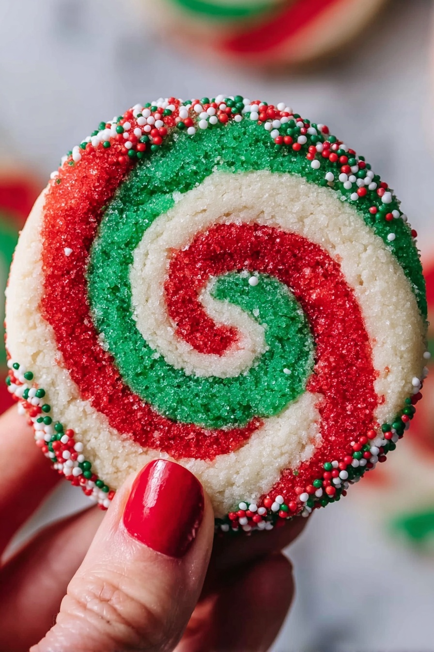 A round cookie with a red, white, and green swirl pattern that forms a spiral from the center to the edges. The outer edge of the cookie is coated with small red, white, and green round sprinkles. A woman's hand with red nail polish holds the cookie against a blurred background, and the surface under the cookie is white marbled texture. photo taken with an iphone --ar 2:3 --v 7 - Swirled Christmas Cookies, festive holiday cookies, holiday cookie recipes, colorful Christmas cookies, buttery holiday treats