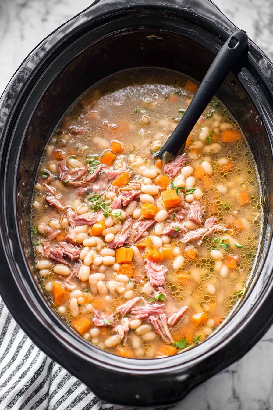 A large black slow cooker filled with a stew that has several layers and textures. The base layer shows a light brown broth with small bubbles of oil floating on top. Floating in the broth are many small, soft white beans, many small orange carrot cubes, and small bits of translucent onions. There are also shredded pieces of pinkish-brown cooked meat spread evenly throughout. Small green herbs are scattered on top, adding a fresh touch. A black spoon is partially submerged on the left side, resting inside the slow cooker. The slow cooker sits on a white marbled surface with a striped cloth partially visible below. Photo taken with an iphone --ar 2:3 --v 7 - Hearty Ham and Bean Soup, hearty ham and bean soup, easy ham and bean soup, comforting bean soup recipe, slow cooker ham and bean soup