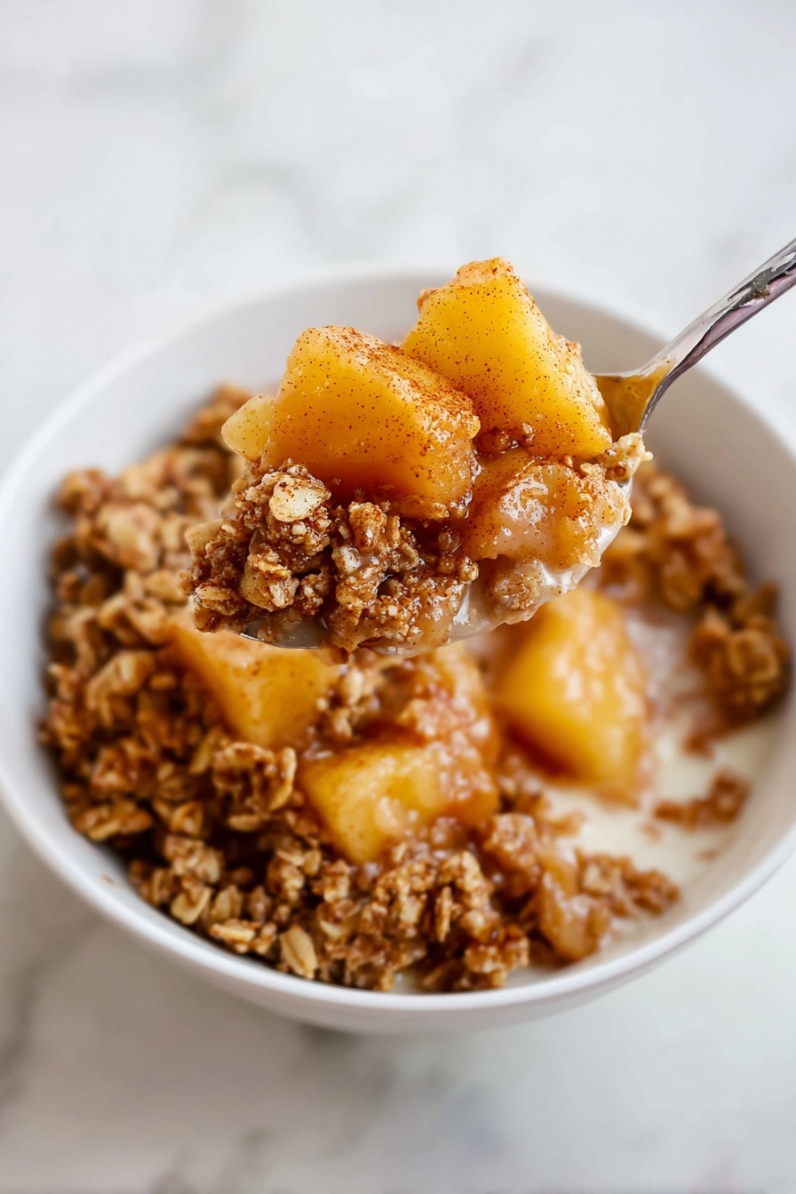 A white bowl filled with a layered dessert of breakfast granola and soft cooked fruit pieces. The bottom layer has light brown granola clusters with a crunchy texture. On top, there are chunks of yellowish-orange cooked fruit, likely pears or apples, coated with a light cinnamon dusting. A spoon scoops a mix of both the soft fruit and granola from the bowl, held close to the camera. The background surface is a white marbled texture. Photo taken with an iphone --ar 2:3 --v 7 - Healthy Apple Crumble Breakfast, wholesome apple crumble breakfast, nutritious apple crumbled dish, healthy morning apple dessert, easy healthy breakfast with apples