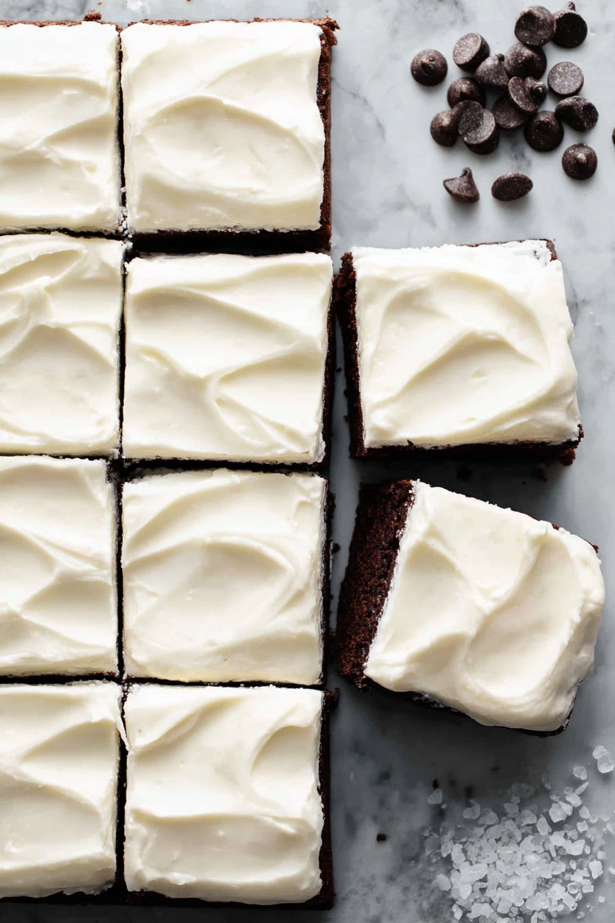 The image shows a dark brown chocolate cake cut into 12 square pieces, nine still together on the left side, and three separated on the white marbled textured surface to the right. Each square has a thick, smooth layer of white cream frosting on top, with gentle swirls creating a soft texture. A few dark chocolate chips are scattered at the top right corner, and some small white salt crystals are near the bottom right edge. The overall look is clean and inviting, with the contrast between the rich dark cake and the bright white frosting clearly visible. photo taken with an iphone --ar 2:3 --v 7 - Baileys Irish Cream Brownies, Irish Cream Brownies, Boozy Brownie Recipes, Fudgy Baileys Brownies, Best Baileys Brownies