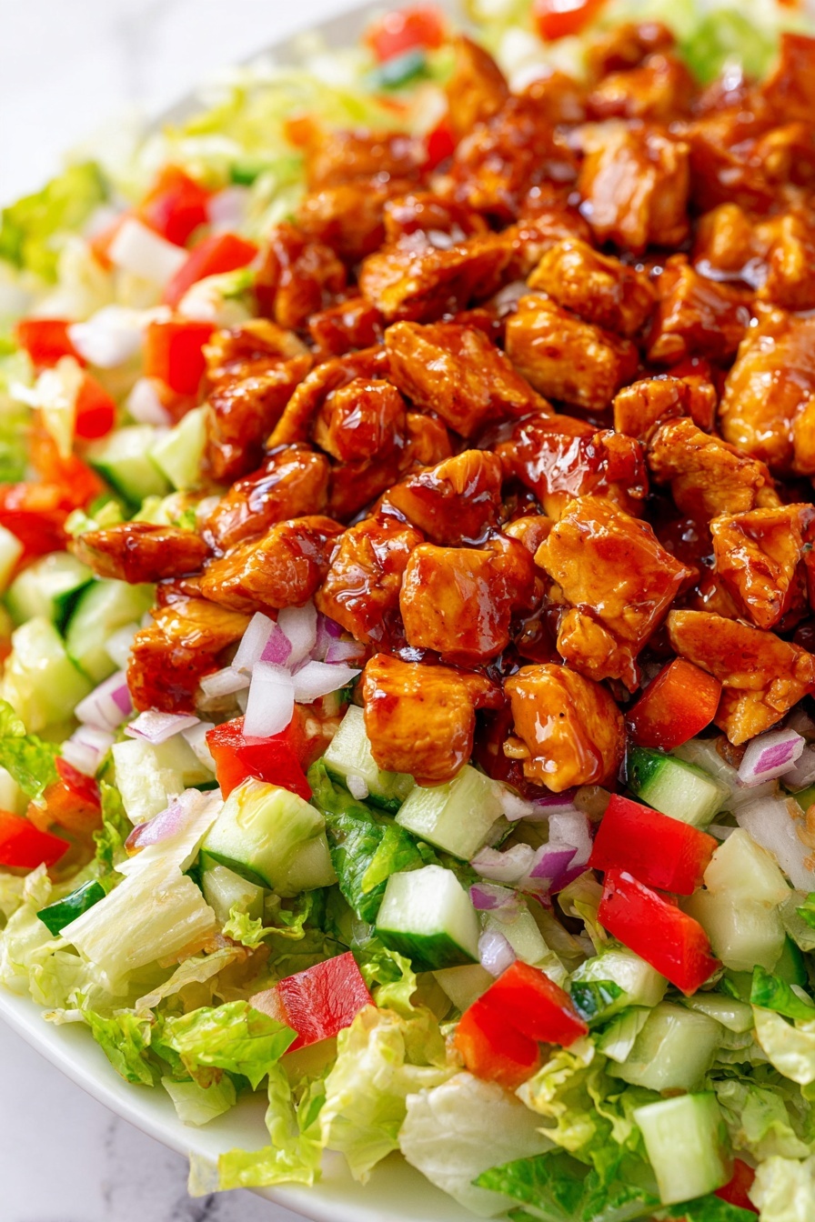 The dish shows a close-up of a salad on a white plate with a white marbled background. The bottom layer has bright green chopped lettuce with a light, crisp texture. Over the lettuce, there are small diced pieces of red bell pepper and white chopped onion spread evenly, adding red and white colors. There are also small cubes of green cucumber scattered throughout this layer. Finally, the top layer consists of chunks of chicken coated in a shiny reddish-brown sauce, giving the salad a rich, glazed look. Photo taken with an iphone --ar 2:3 --v 7 - Honey Hot Chicken Salad, spicy chicken salad, buffalo chicken salad, easy chicken salad recipes, quick lunch ideas